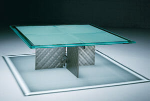 Radian Coffee Table with Buffed Steel leg texture and a Clear Glass top with beveled edge.